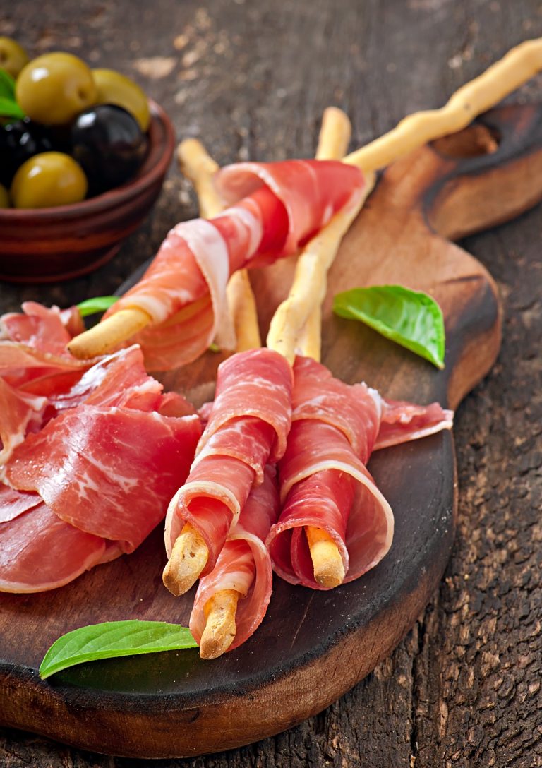 Grissini bread sticks with ham, olives, basil on old wooden background