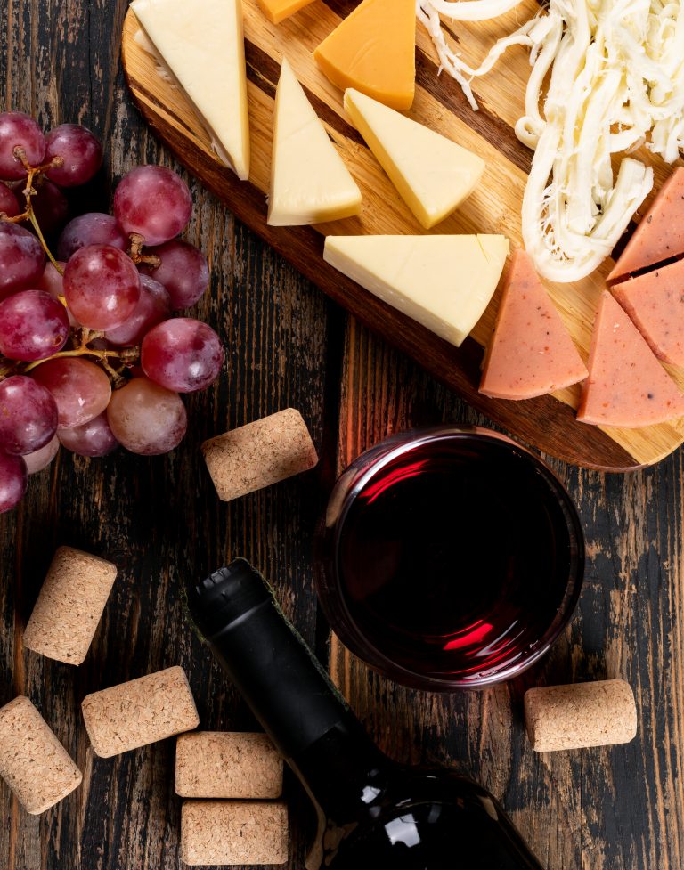 top-view-red-wine-with-grape-cheese-cutting-board-dark-wooden-vertical